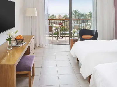 a hotel room with a bed and a television and a balcony at Mövenpick Resort & Spa Tala Bay Aqaba in Aqaba