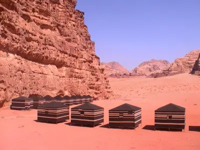 a group of tents in the desert near a cliff at Jordan Tracks Bedouin Camp in Wadi Rum
