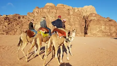 a group of people riding camels in the desert at Jordan Tracks Bedouin Camp in Wadi Rum