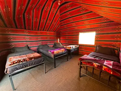a room with three beds and a red wall at Desert Bird Camp in Wadi Rum