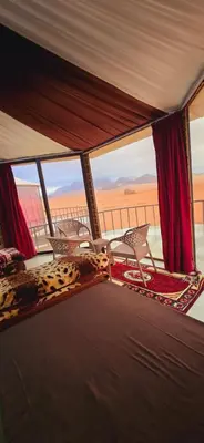a room with chairs and a balcony with a view of the desert at Wadi Rum Candles Camp in Wadi Rum
