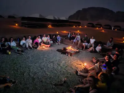 a group of people sitting around a fire pit at night at Wadi Rum Candles Camp in Wadi Rum