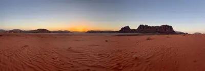 a desert with the sun setting in the background at Rumshines Camp in Wadi Rum