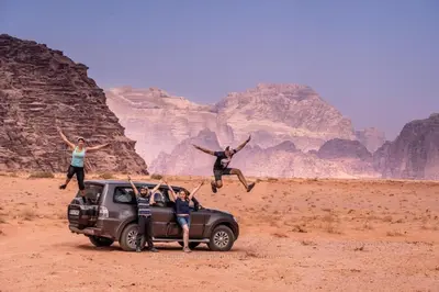 a group of people jumping off of a car in the desert at Wild of Wadi Rum in Wadi Rum