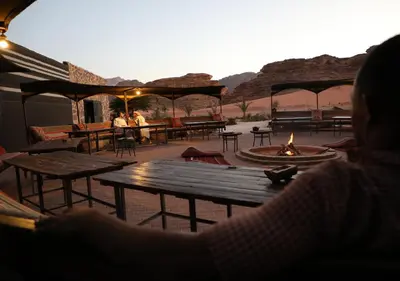 a woman sitting at a picnic table with a fire at Rum Planet Camp in Wadi Rum