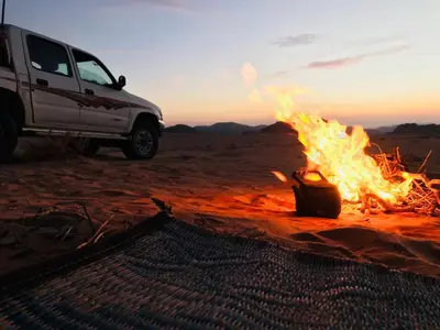 a fire in the middle of the desert with a truck at Red Mountain Camp in Wadi Rum