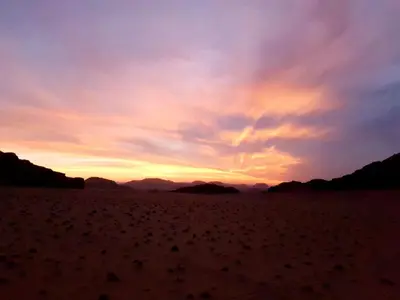 a sunset in the desert with mountains in the background at Wadi Rum Nature Tours And Camp in Wadi Rum
