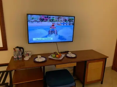 a television on a wall with a table with a plate of fruit at Marina Plaza Hotel, Tala Bay in Aqaba