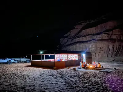 a group of people sitting around a fire at night at Wadi Rum Jordan Camp in Wadi Rum