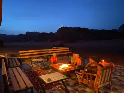 a group of people sitting around a fire at night at Wadi Rum Jordan Camp in Wadi Rum