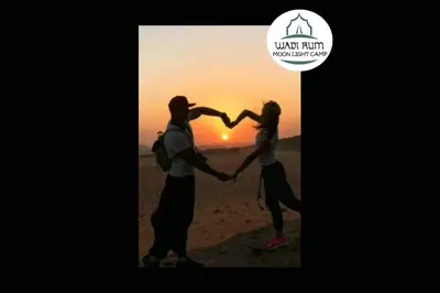a man and woman holding hands while standing in front of a sunset at Wadi Rum Moon Light Camp in Wadi Rum