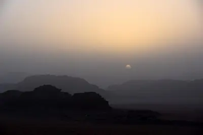 a misty view of the sun setting over mountains at Wadi Rum Fire Camp in Wadi Rum