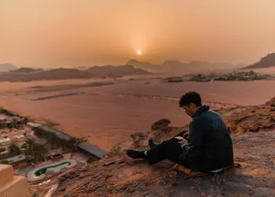 a man sitting on a rock looking at the sunset at Bait Ali in Wadi Rum