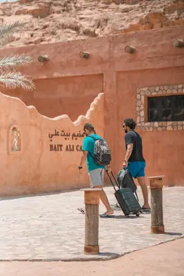 two people with luggage walking in front of a building at Bait Ali in Wadi Rum