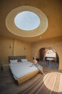 a woman is sitting on a bed in a room with a window at Bait Ali in Wadi Rum