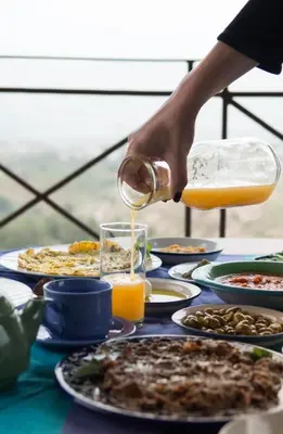 a person pouring orange juice onto a table of food at Beit Al Fannan in Ţabaqat Faḩl