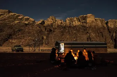 a group of people sitting around a fire in front of a mountain at Arabian Nights in Wadi Rum