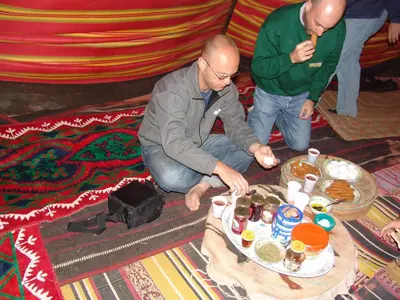 two men sitting on the floor with a table with food at Climbers House in Wadi Rum in Wadi Rum
