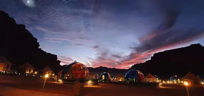 a group of domed buildings at night with a sunset at Memories Aicha Luxury Camp in Wadi Rum