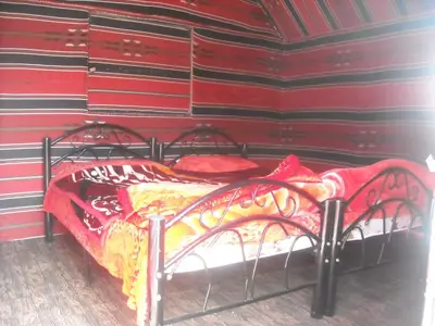 a bedroom with a bed with red sheets and red pillows at Bedouin House Camp in Wadi Rum