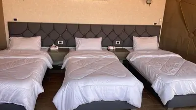 three beds in a room with white sheets and pillows at Black Irish Camp And Tours in Wadi Rum
