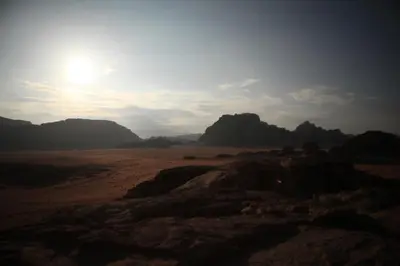 a view of a desert with mountains and the sun at Bedouin Expedition in Wadi Rum