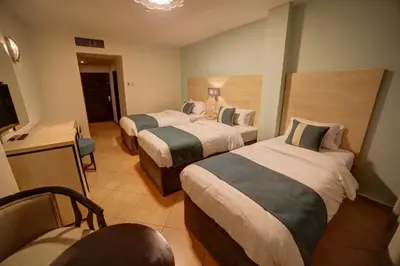 a hotel room with three beds and a television at Crystal Hotel By FHM in Aqaba