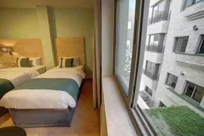 two beds in a room with a large window at Crystal Hotel By FHM in Aqaba