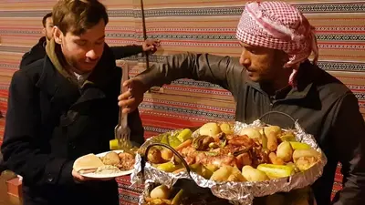 two men standing next to a table with a plate of food at Real Bedouin Experience Tours & Camp in Wadi Rum