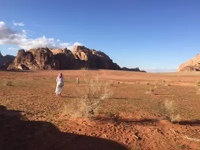 a woman walking through a desert with a mountain in the background at WADI RUM-Bedouin Tents and Jeep Tours in Wadi Rum