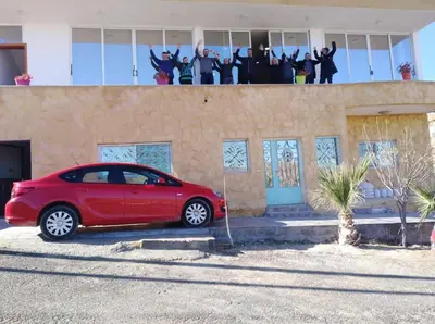 a red car parked in front of a building with people at Jordan Guest House in Wadi Musa