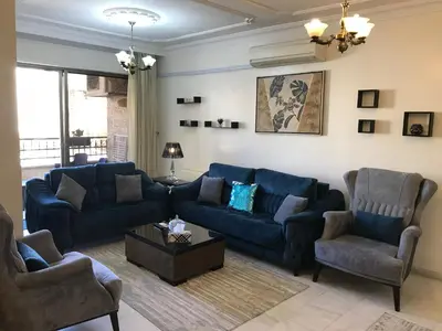 a living room with a blue couch and two chairs at Behind Mecca Mall in Amman