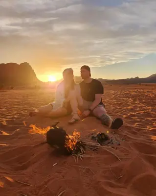 a man and woman sitting next to a fire on the beach at RUM SOlARIS BEDOUIN CAMP in Wadi Rum