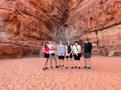a group of people standing in front of a cliff at Star City Camp wadirum in Wadi Rum