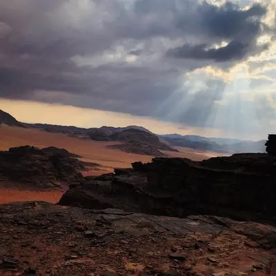 a view of a desert with the sun shining through the clouds at Wadi Rum Excursions in Wadi Rum