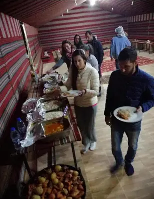 a group of people walking around a buffet with plates of food at Wadi rum Local guide camp in Wadi Rum