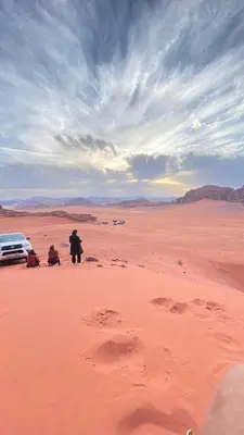 a person standing in the desert with a car at Wadi Rum Pyramids Camp in Wadi Rum
