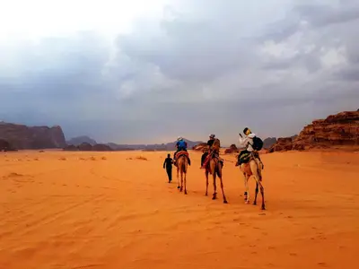a group of people riding camels in the desert at Landscape Rum Camp in Wadi Rum