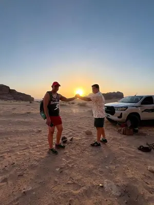 two men standing in front of a car in the desert at Moon city camp in Wadi Rum