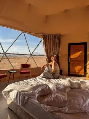 a woman sitting on a bed in front of a window at Taj Wadi Rum camp in Wadi Rum