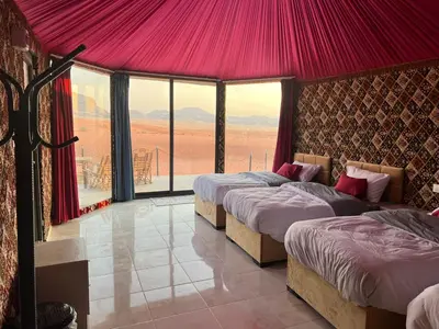 three beds in a room with a view of the desert at Wadi Rum Desert Adventures in Wadi Rum
