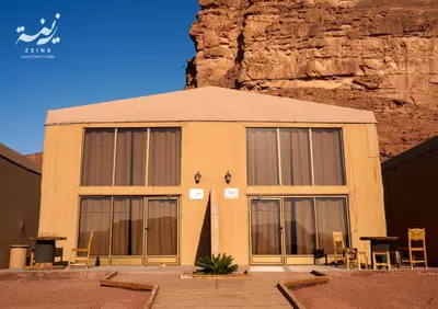 a building with large windows in front of a mountain at Zeina Desert Lodge in Wadi Rum