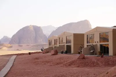 a building in the desert with mountains in the background at Zeina Desert Lodge in Wadi Rum