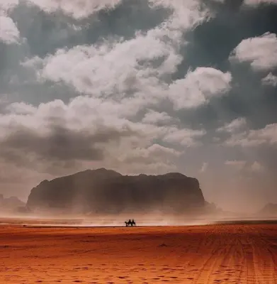 two people riding horses in the desert under a cloudy sky at Desert shine camp in Wadi Rum