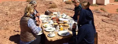a group of people standing around a table in the desert at Discover the life of Wadi Rum camp in Wadi Rum