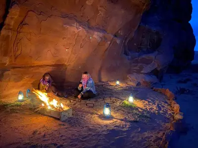 two people sitting around a fire in a cave with candles at Wadi Rum night soul Camp in Wadi Rum