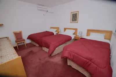 three beds in a room with red covers on them at Petra Lion Hotel in Wadi Musa