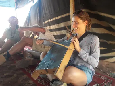 a woman is smiling while holding a wooden object at WadiRum Mobile Camp in Wadi Rum