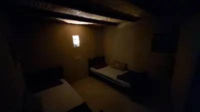 a dark room with two beds and a window at Wadi Ghwere Camp مخيم وادي الغوير in Al Khuraybah