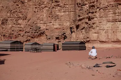 a man sitting on the sand in front of a cliff at Wadirum momoo in Wadi Rum